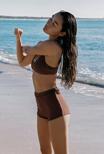 Woman in a brown bikini standing on a beach with ocean in the background